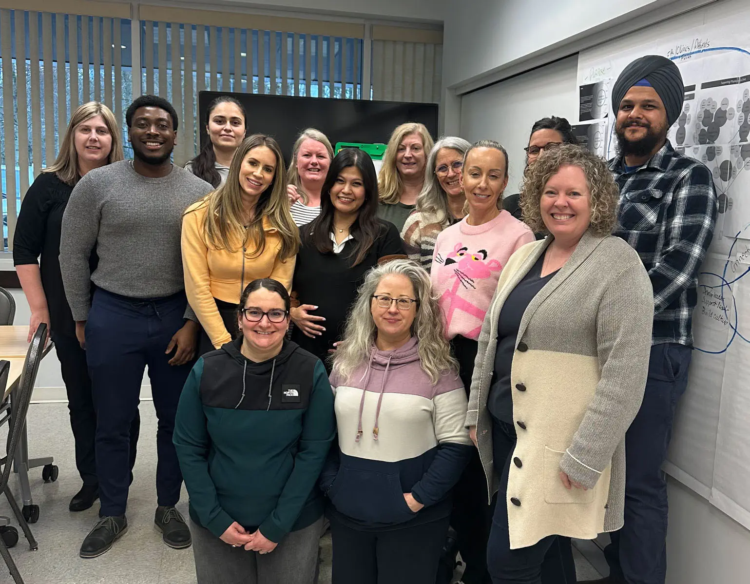 Group photo of the 2024 team from White Rock South Surrey Division of Family Practice, standing together in a meeting room with diagrams on the wall.