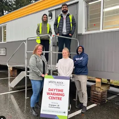 Team members standing outside the Daytime Warming Centre in South Surrey White Rock, with a sign in the foreground indicating community engagement