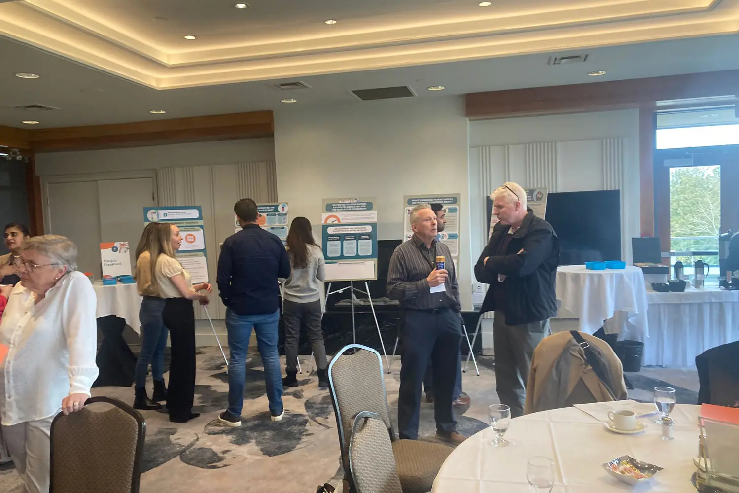 Team members and attendees networking and discussing healthcare topics at a professional event in South Surrey White Rock, with informational posters displayed in the background