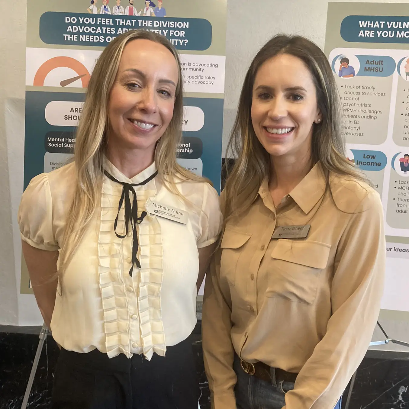 Two of our team members posing in front of informational posters at a healthcare event in South Surrey White Rock.